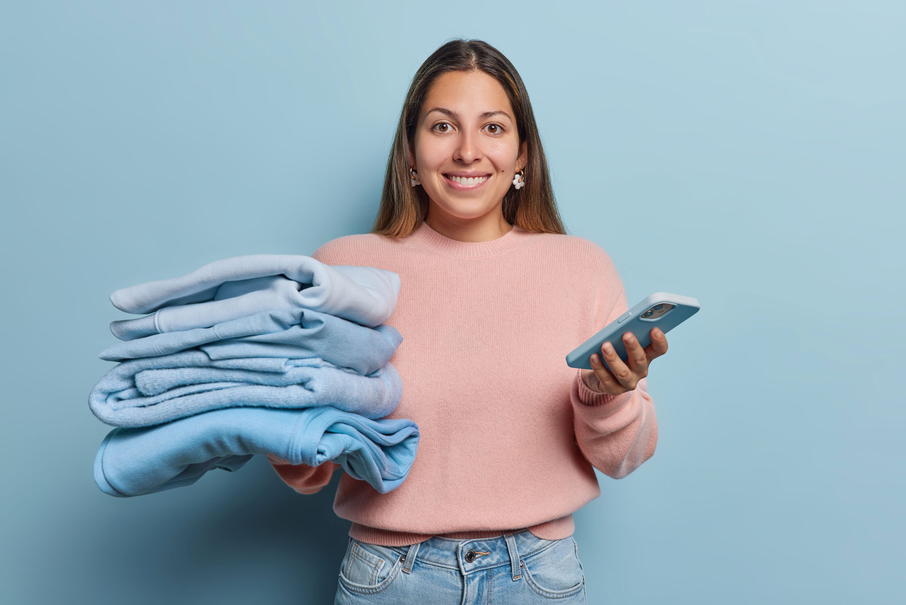 Persona sosteniendo una pila de ropa recién doblada y un teléfono