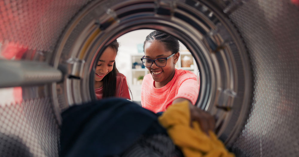View from inside a washing machine drum of two people loading laundry at EveryBuddy's Laundromat