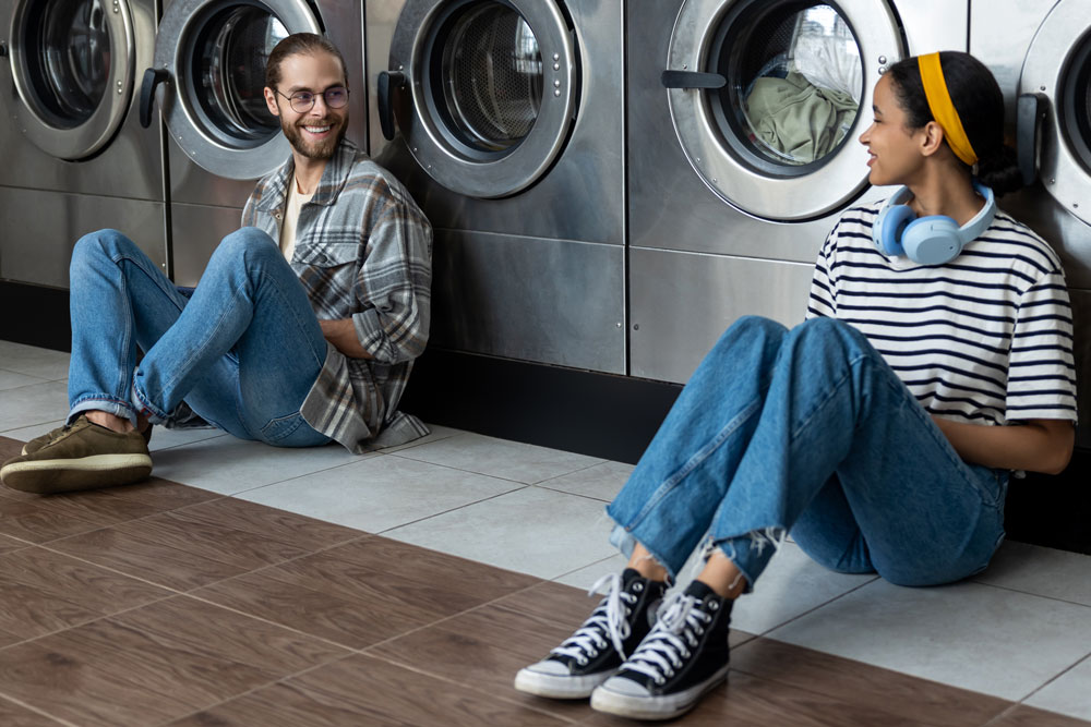 Two people chatting while waiting in front of a row of washing machines at EveryBuddy's Laundromat