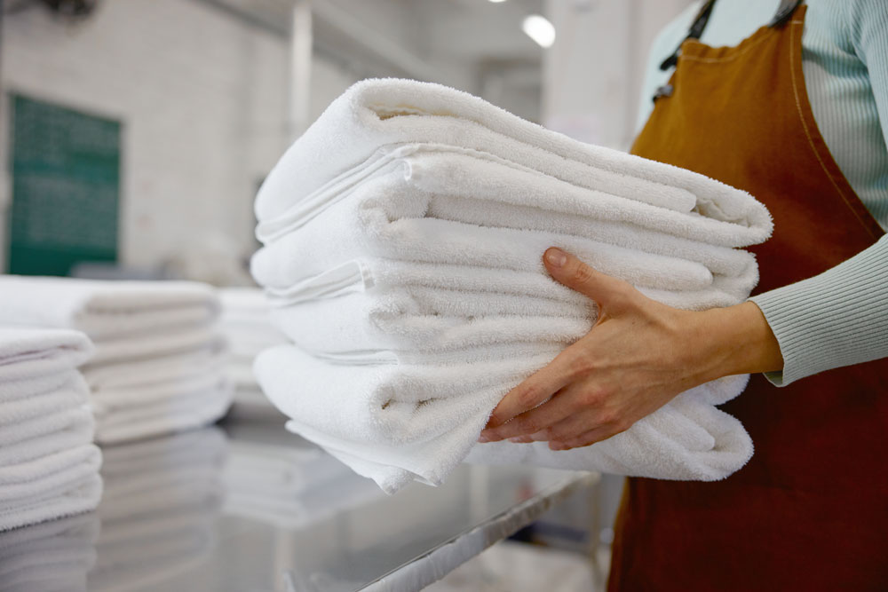 Attendant holding a stack of folded white towels at EveryBuddy's Laundromat