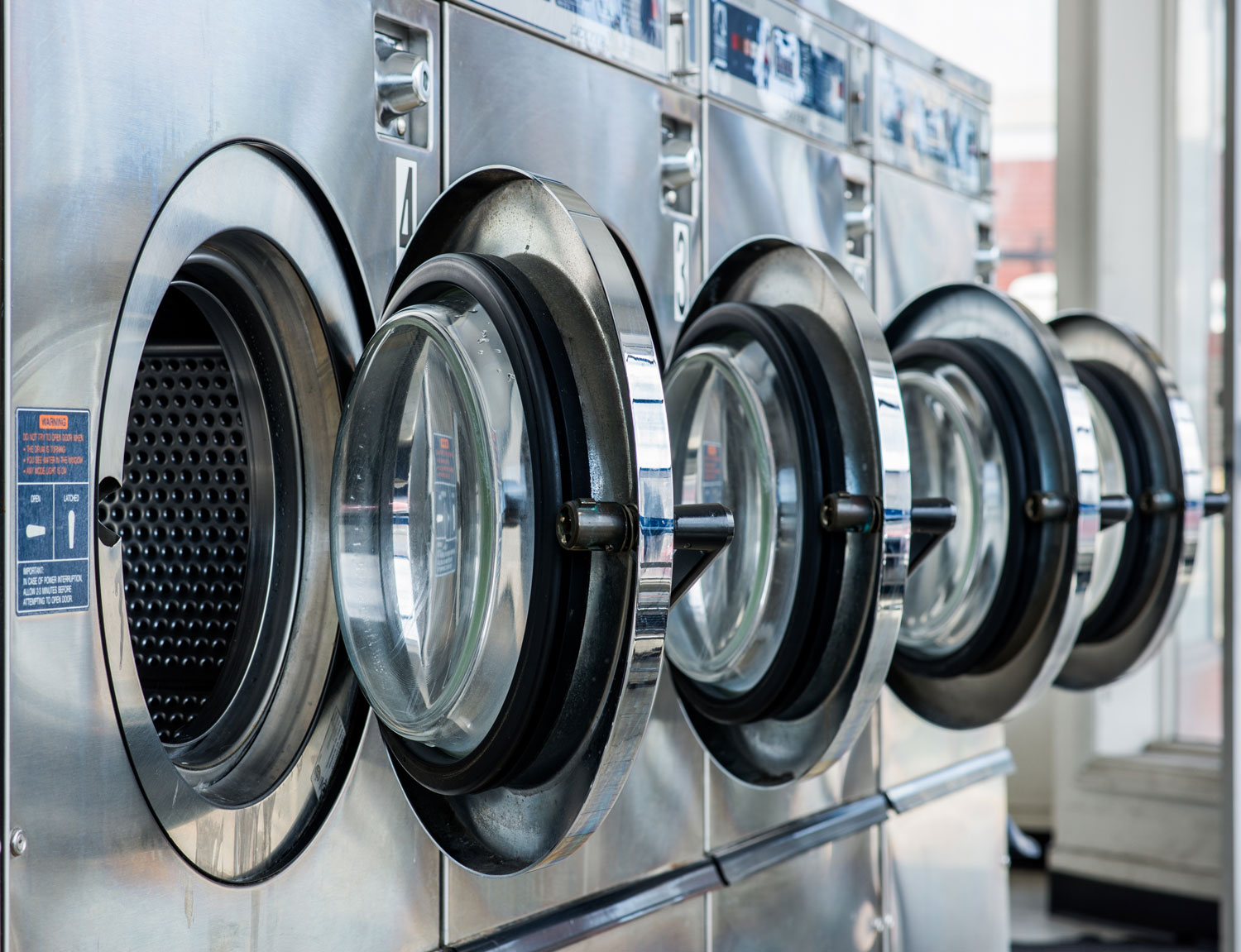 Row of stainless steel front-load washing machines at EveryBuddy's Laundromat