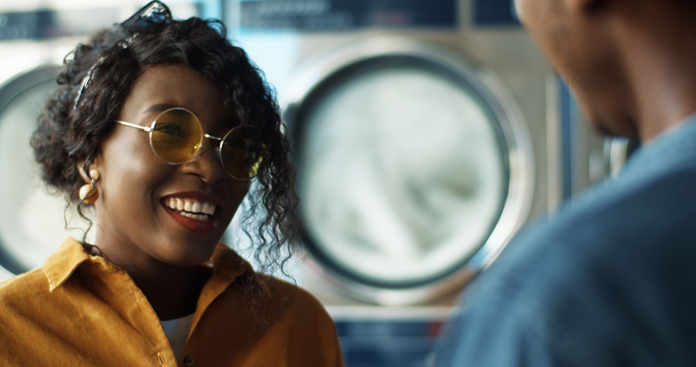 Two people smiling and talking in front of washing machines at EveryBuddy's Laundromat
